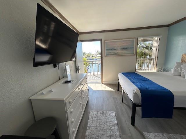 A bedroom features a wall-mounted television, a white dresser, and a bed near a balcony — 7150 N TAMIAMI TRAIL UNIT C233, SARASOTA, FL