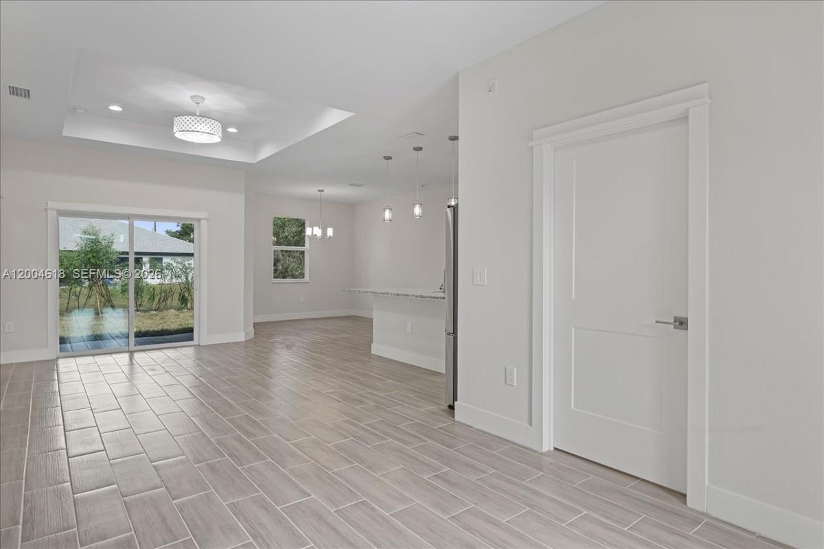 A bright, open-concept living area features light wood-look tile flooring and a sliding glass door — 2804 11th ST W, Lehigh Acres FL 33971, LEHIGH ACRES, FL