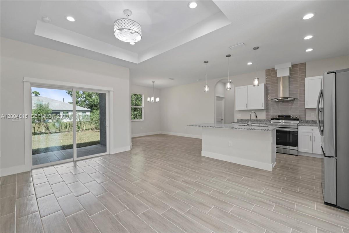 An open-concept kitchen and dining area features light wood-look tile floors and a tray ceiling — 2804 11th ST W, Lehigh Acres FL 33971, LEHIGH ACRES, FL