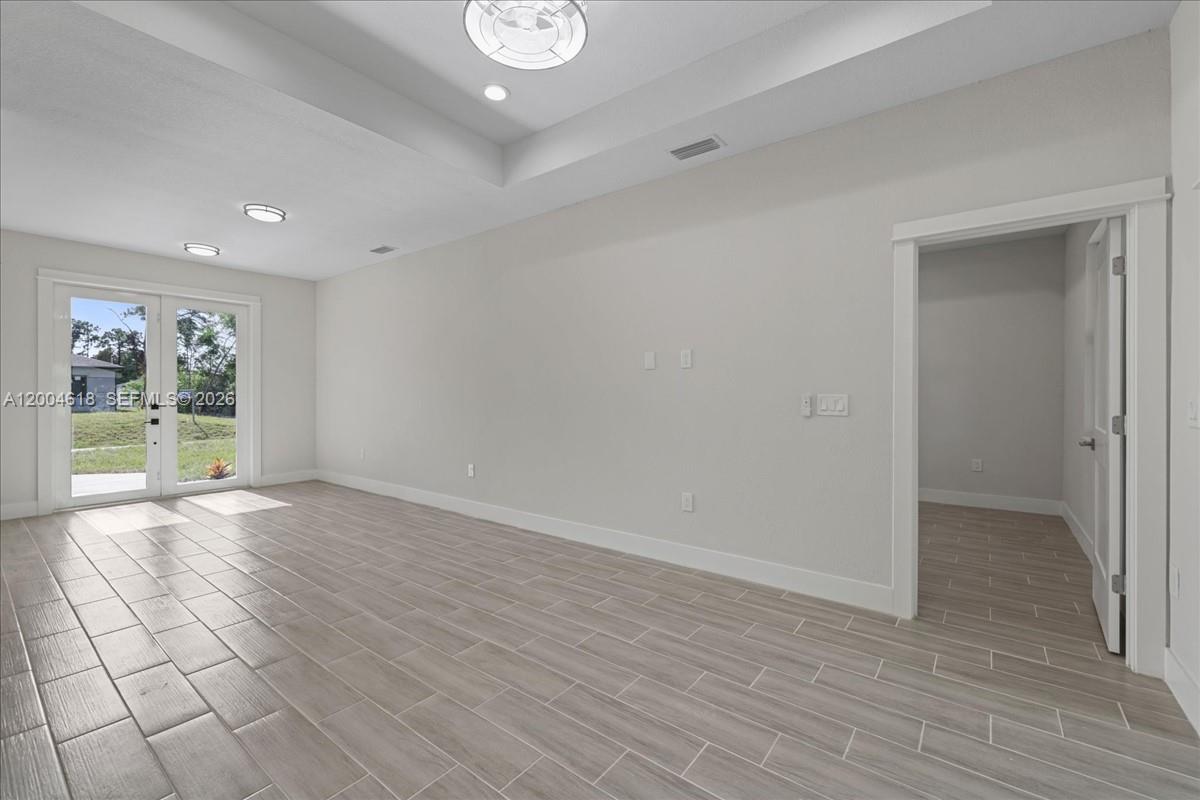 An empty room features light wood-look tile flooring, a tray ceiling, and glass double doors — 2804 11th ST W, Lehigh Acres FL 33971, LEHIGH ACRES, FL