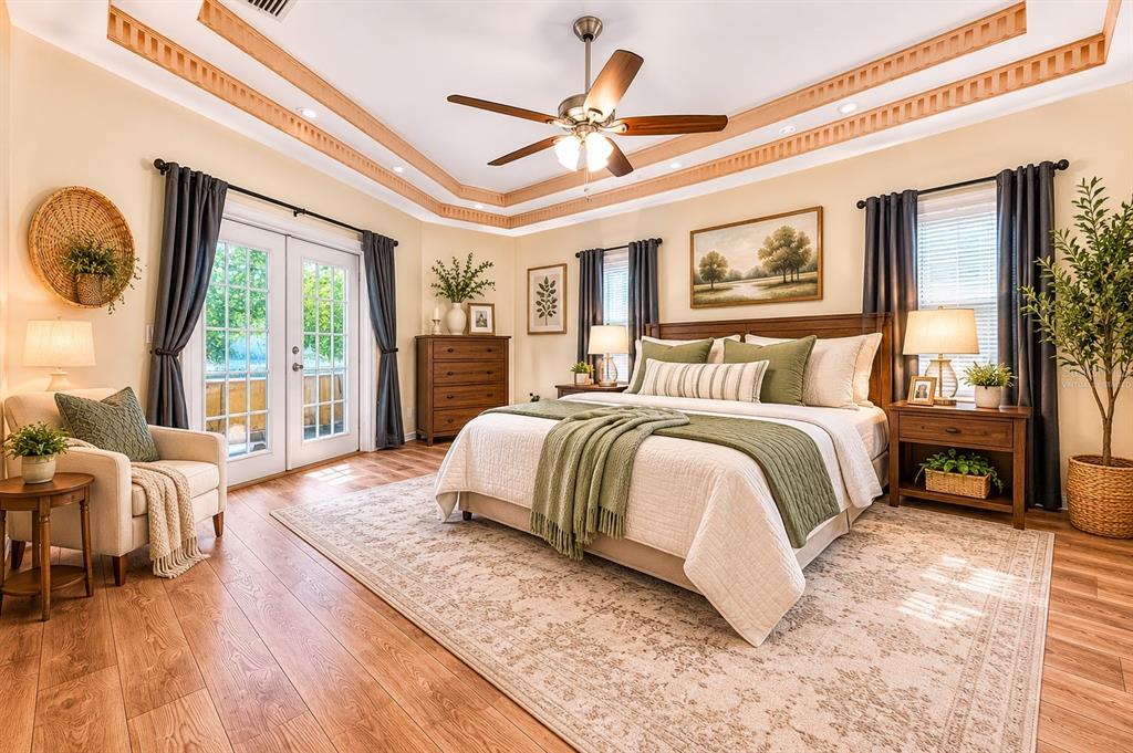 A bedroom features a tray ceiling, a king-sized bed, wood flooring, and glass patio doors — 7222 STANFORD DR, LAKELAND, FL