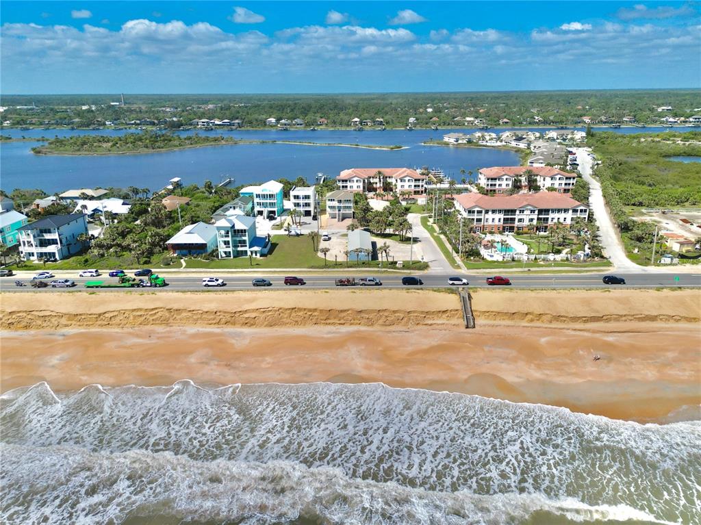 An aerial view shows a coastal road separating a sandy beach from waterfront residential buildings — 2299 N OCEANSHORE BOULEVARD, FLAGLER BEACH, FL