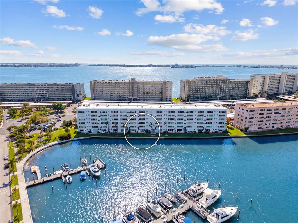 An aerial view shows multi-story apartment buildings, a marina, and parking lots at sunset — 5925 SHORE BOULEVARD S UNIT 108, GULFPORT, FL