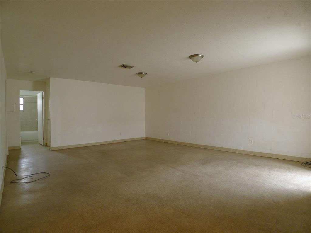 An empty room with beige carpet, white walls, and a doorway leading to a bathroom — 3420 N 55TH STREET UNIT B, TAMPA, FL