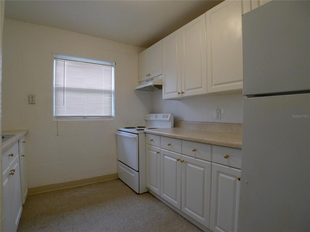 A kitchen features white cabinets, a white stove, a refrigerator, and a window with blinds — 3420 N 55TH STREET UNIT B, TAMPA, FL