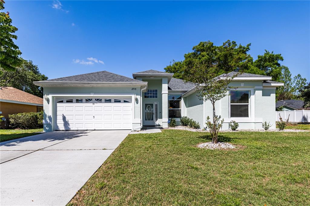 A single-story house with a white garage, light green stucco exterior, and a front lawn — 2710 AUTUMN LANE, EUSTIS, FL