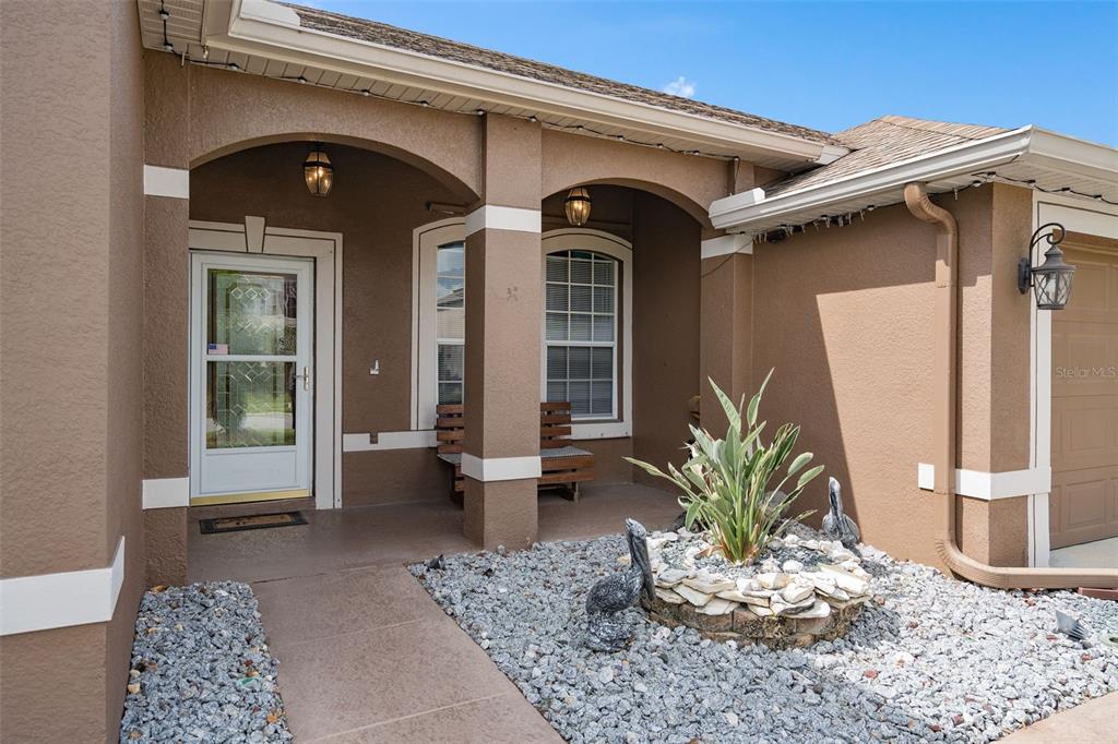 A tan stucco house exterior features a covered entryway, a stone garden, and two pelican statues — 726 SENECA MEADOWS ROAD, WINTER SPRINGS, FL