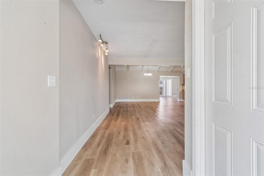A spacious living room with light wood-look flooring flows into an open kitchen with cabinets — 13691 SERENA DRIVE, LARGO, FL