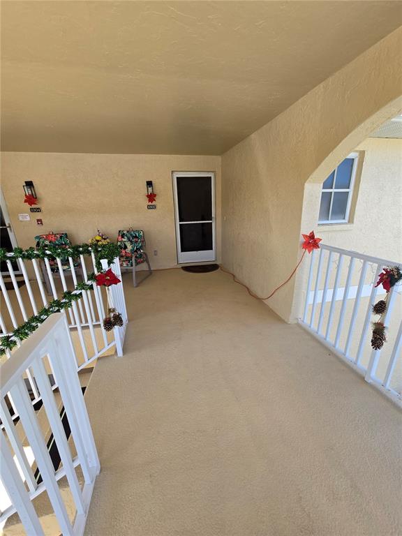 An outdoor covered walkway features white railings, two chairs, and holiday decorations — 5800 SABAL TRACE DRIVE UNIT 1002, NORTH PORT, FL