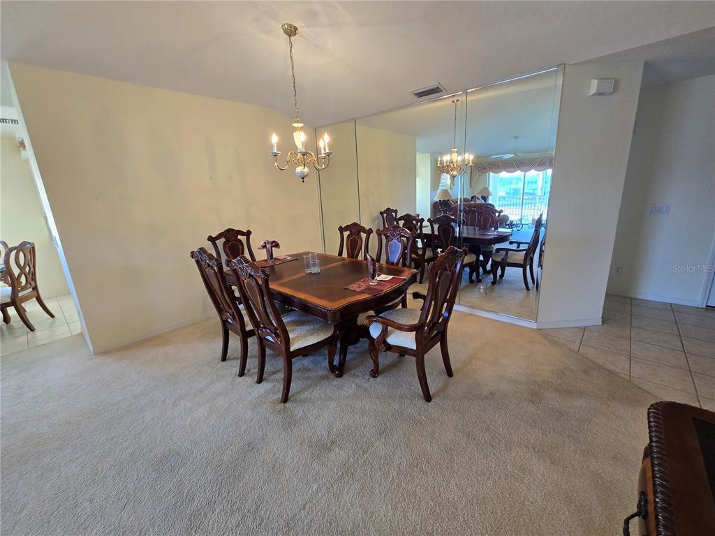 A dining room features a wooden table with chairs, a chandelier, and a mirrored wall — 5800 SABAL TRACE DRIVE UNIT 1002, NORTH PORT, FL