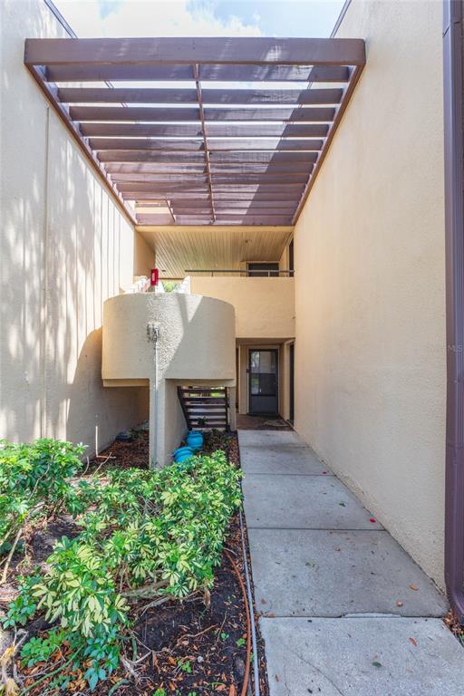 A concrete walkway leads to an entryway beneath a wooden pergola and a curved wall — 895 N VILLAGE DRIVE N UNIT 204, ST PETERSBURG, FL