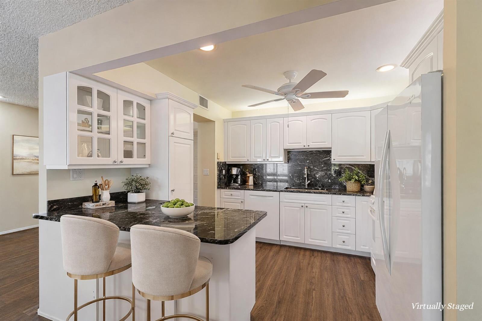 A kitchen features white cabinets, black marble countertops, a ceiling fan, and two bar stools — 1800 SE Saint Lucie Boulevard # 201, Stuart FL 34996, STUART, FL