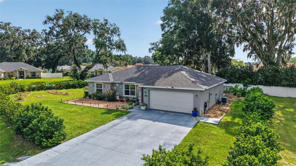 An exterior view of a single-story gray house with a two-car garage and large trees — 10097 SW 78TH COURT, OCALA, FL