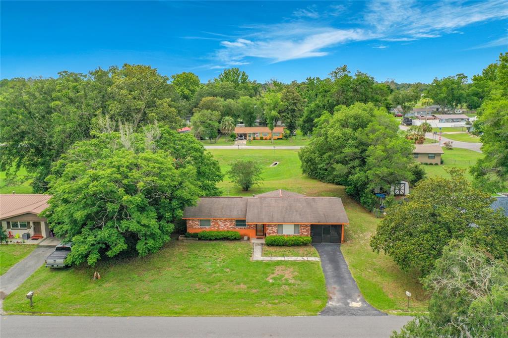 An aerial view shows a single-story brick house with a driveway and large surrounding trees — 910 NE 45TH STREET, OCALA, FL