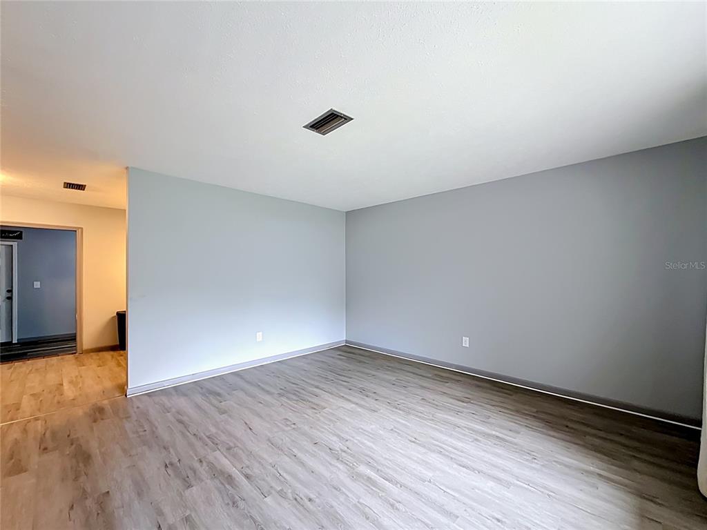 An empty room features gray walls, light wood-look flooring, and a ceiling air vent — 910 NE 45TH STREET, OCALA, FL