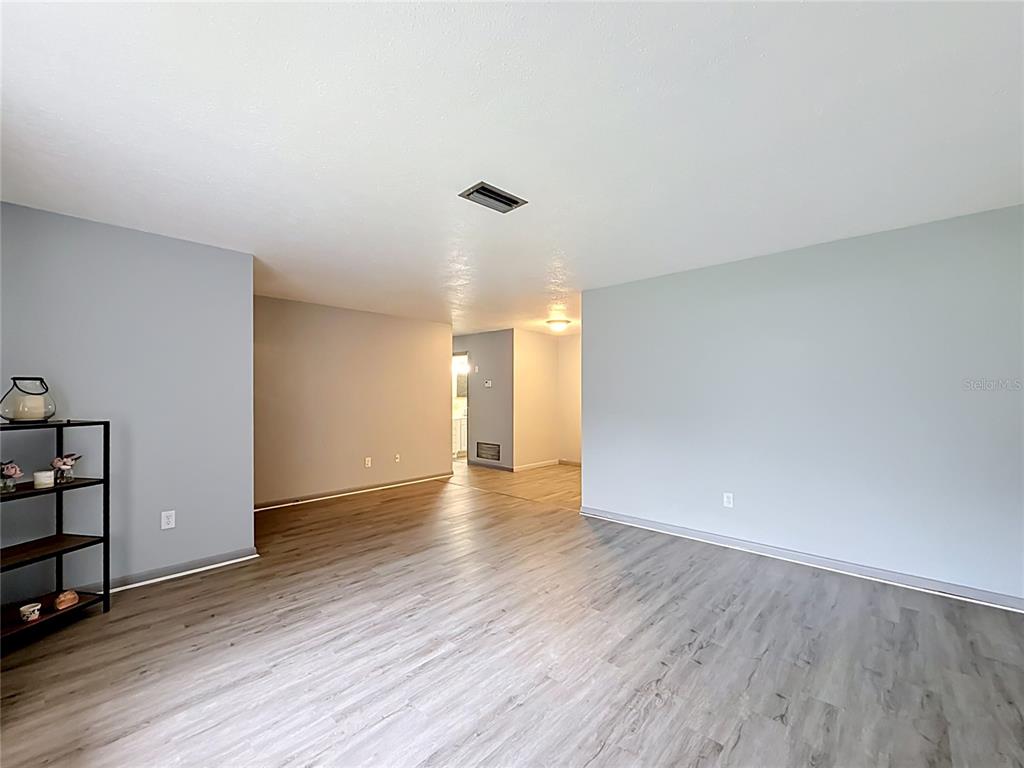 An empty room with light gray walls and wood-look flooring leads to a hallway — 910 NE 45TH STREET, OCALA, FL