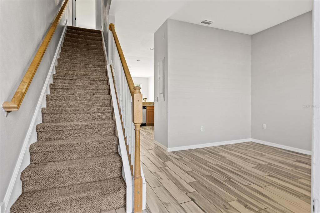 A carpeted staircase with a wooden handrail sits beside a room with wood-look tile flooring — 8874 CHRISTIE DRIVE, LARGO, FL