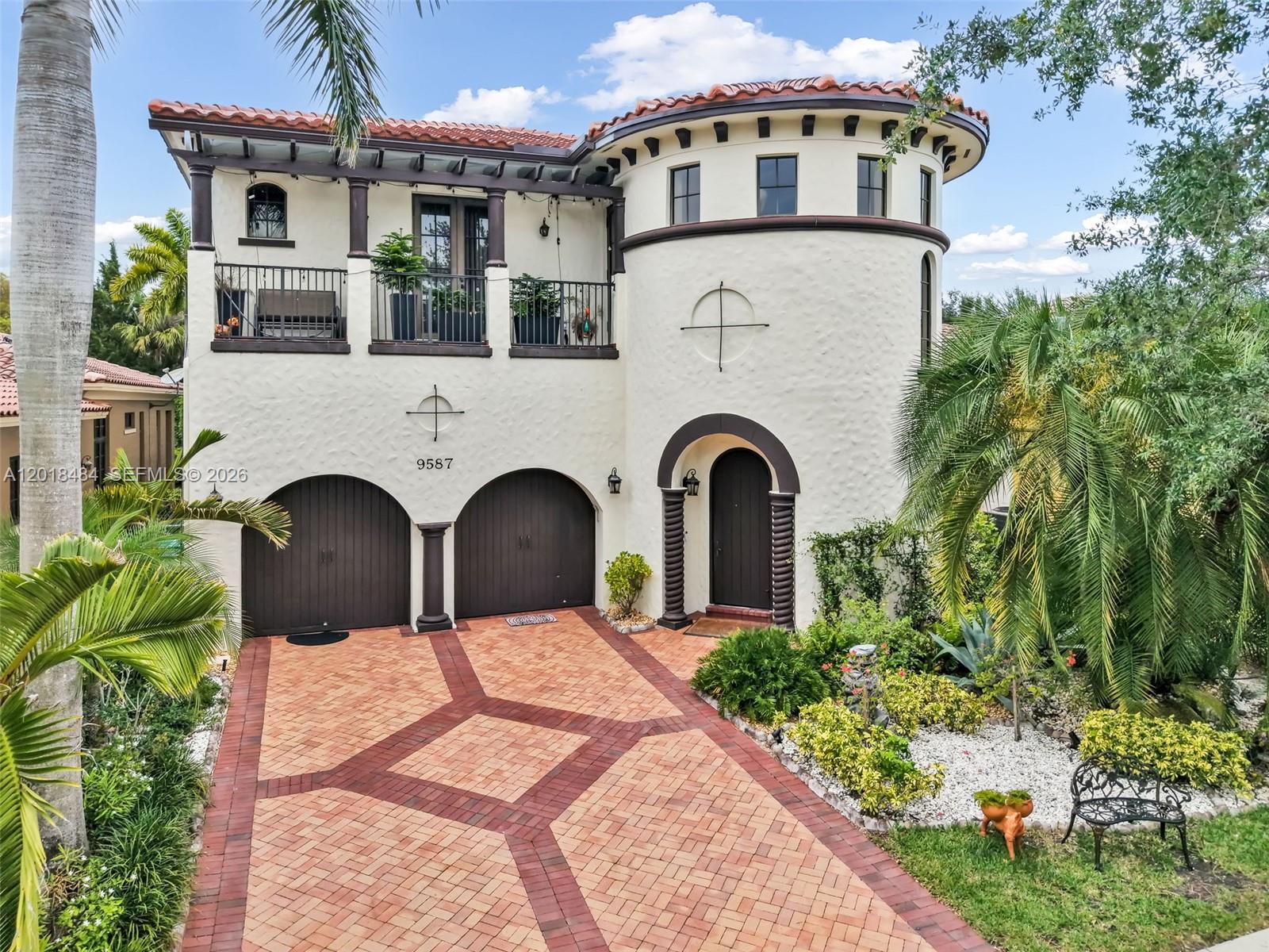 A two-story Mediterranean-style house features a circular tower, arched garage doors, and a balcony — 9587 Exbury Ct, Parkland FL 33076, PARKLAND, FL