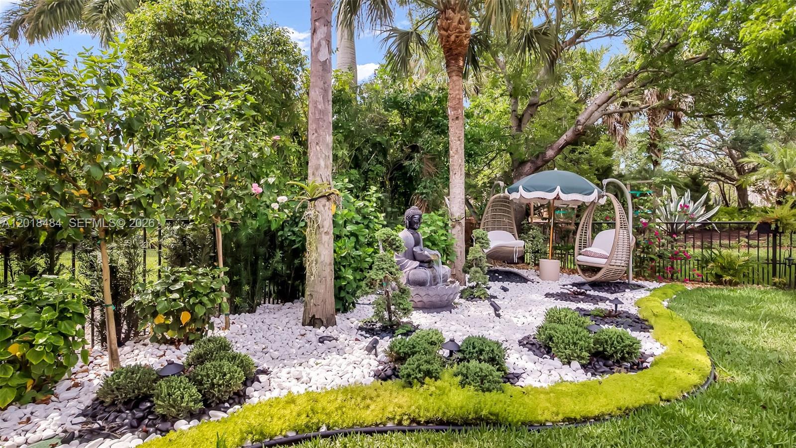 A landscaped garden features a Buddha statue, white gravel, hanging chairs, and lush tropical plants — 9587 Exbury Ct, Parkland FL 33076, PARKLAND, FL