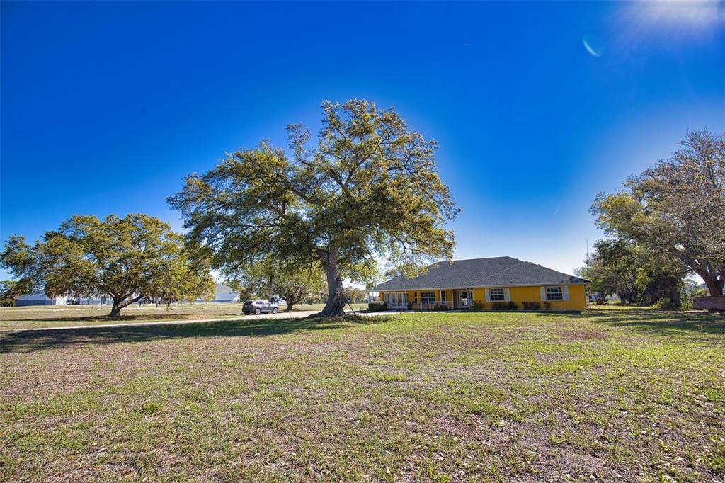 A yellow house sits on a large grassy lot shaded by several mature oak trees — 2820 PAN AMERICAN BOULEVARD, NORTH PORT, FL