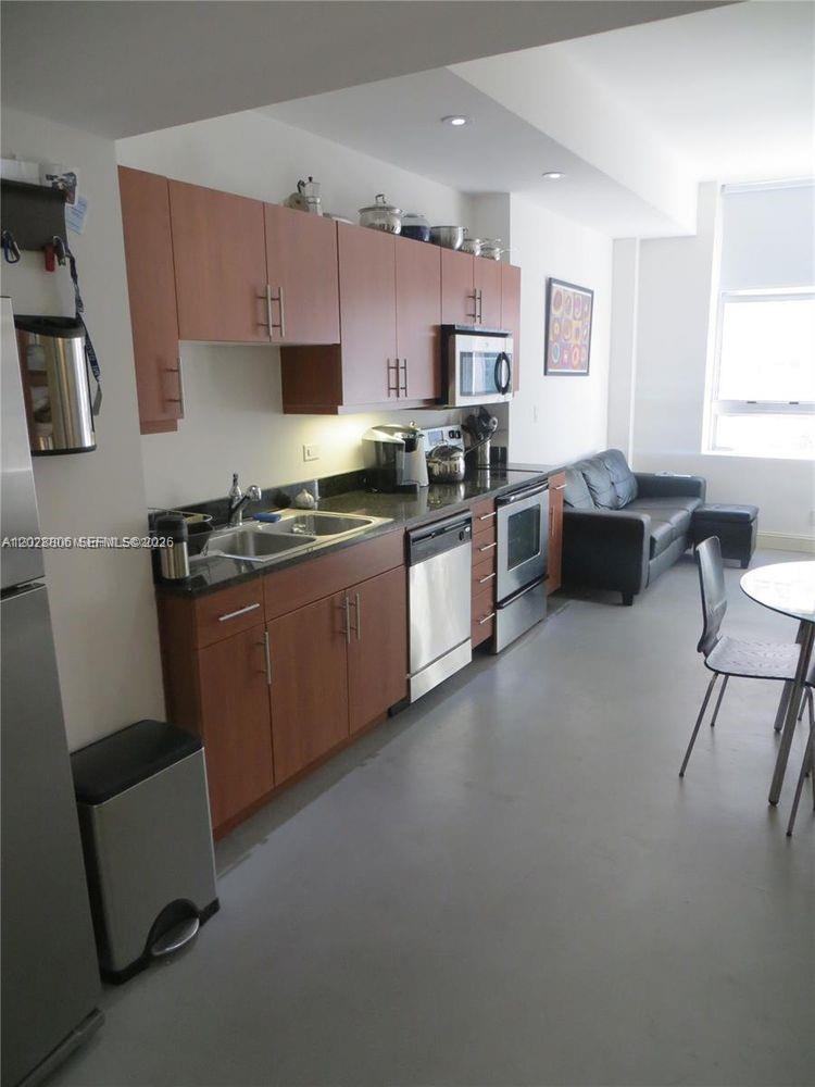 A kitchen with wood cabinets, dark countertops, and stainless steel appliances opens to a living area — 111 E Flagler St # 402, Miami FL 33131, MIAMI, FL