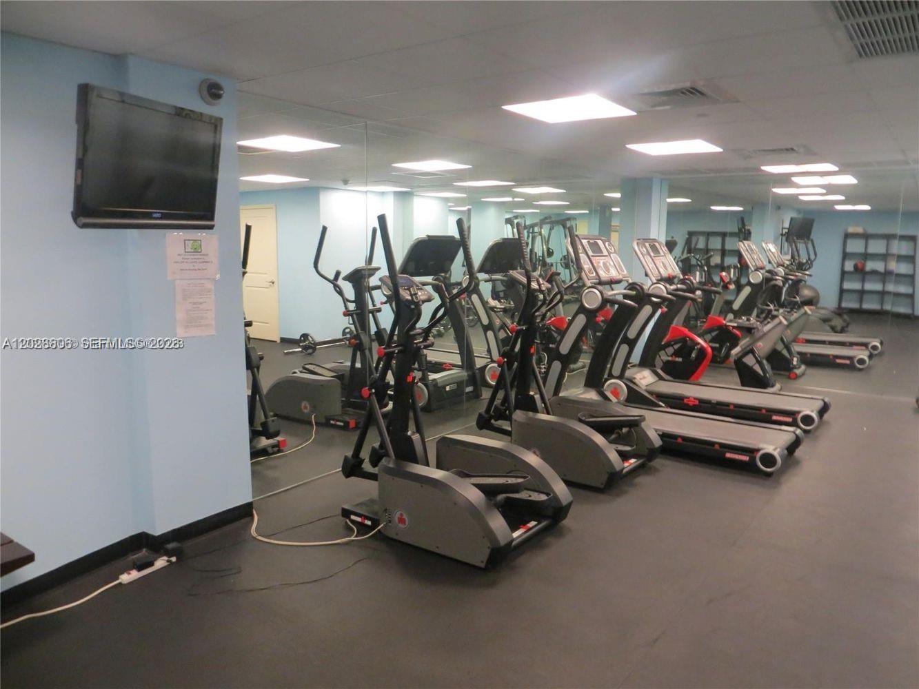A gym room features several elliptical machines and treadmills lined up in front of a mirror — 111 E Flagler St # 402, Miami FL 33131, MIAMI, FL