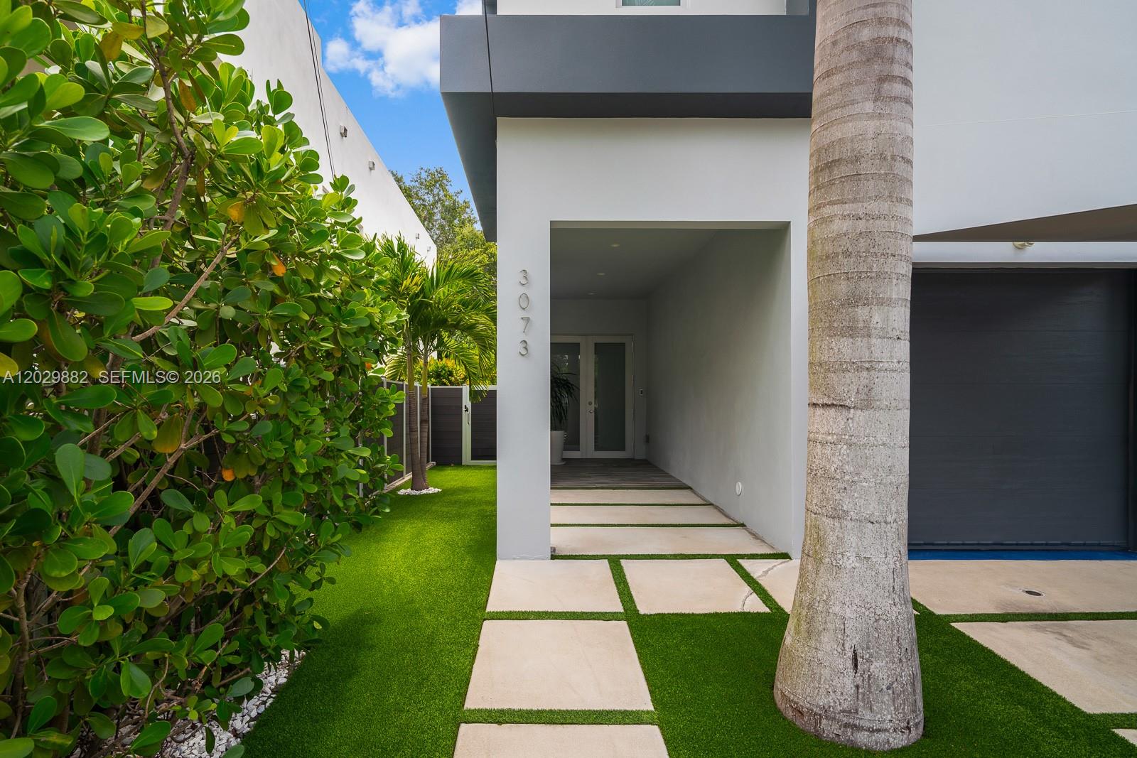 A modern house exterior features a paved walkway, artificial turf, and a palm tree — 3073 Carter St, Miami FL 33133, MIAMI, FL