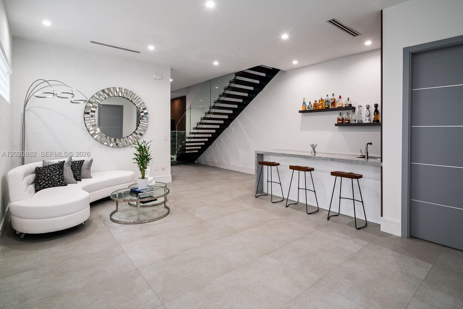 A modern living area features a white curved sofa, a bar with stools, and stairs — 3073 Carter St, Miami FL 33133, MIAMI, FL