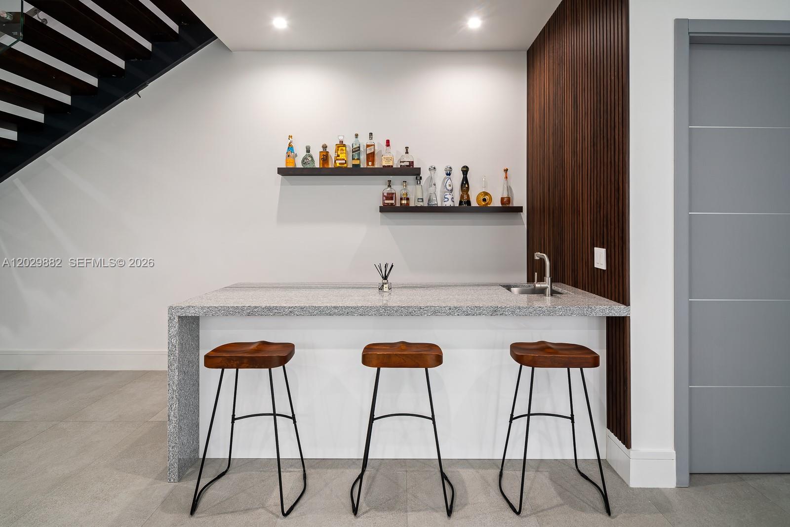 A modern home bar features a granite countertop, three wooden stools, and two floating shelves — 3073 Carter St, Miami FL 33133, MIAMI, FL