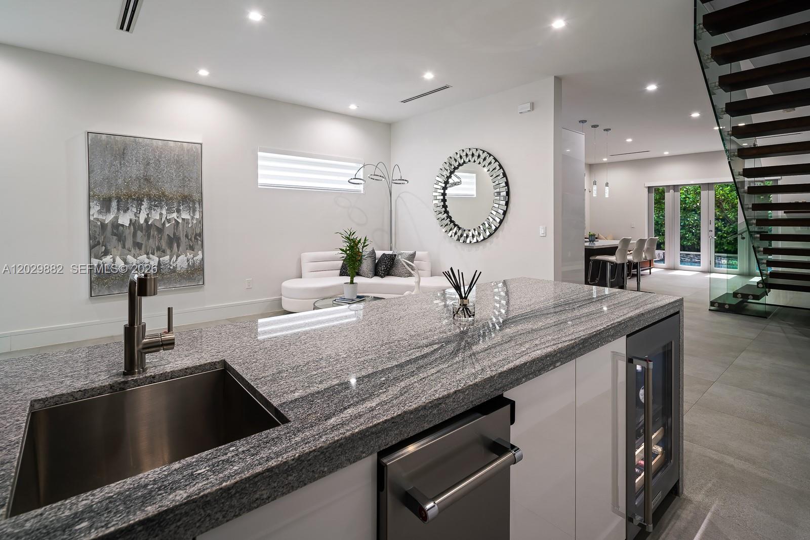 A modern kitchen island with a granite countertop overlooks a living area with white furniture — 3073 Carter St, Miami FL 33133, MIAMI, FL