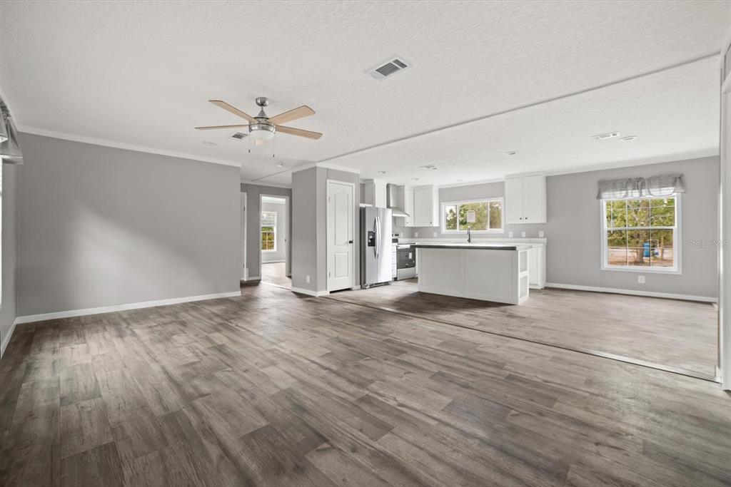 An open-concept living area with gray walls, wood-look flooring, and a kitchen with white cabinets — 20213 NW 258TH STREET, OKEECHOBEE, FL