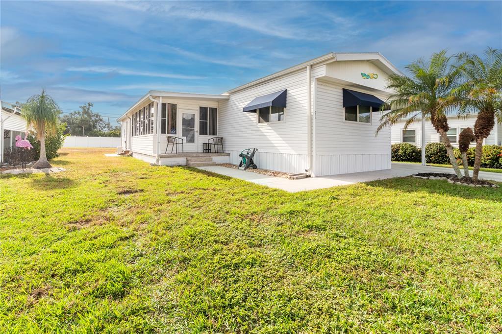 A white mobile home with blue window awnings sits on a grassy lot with palms — 214 LEISURE WAY, PALMETTO, FL