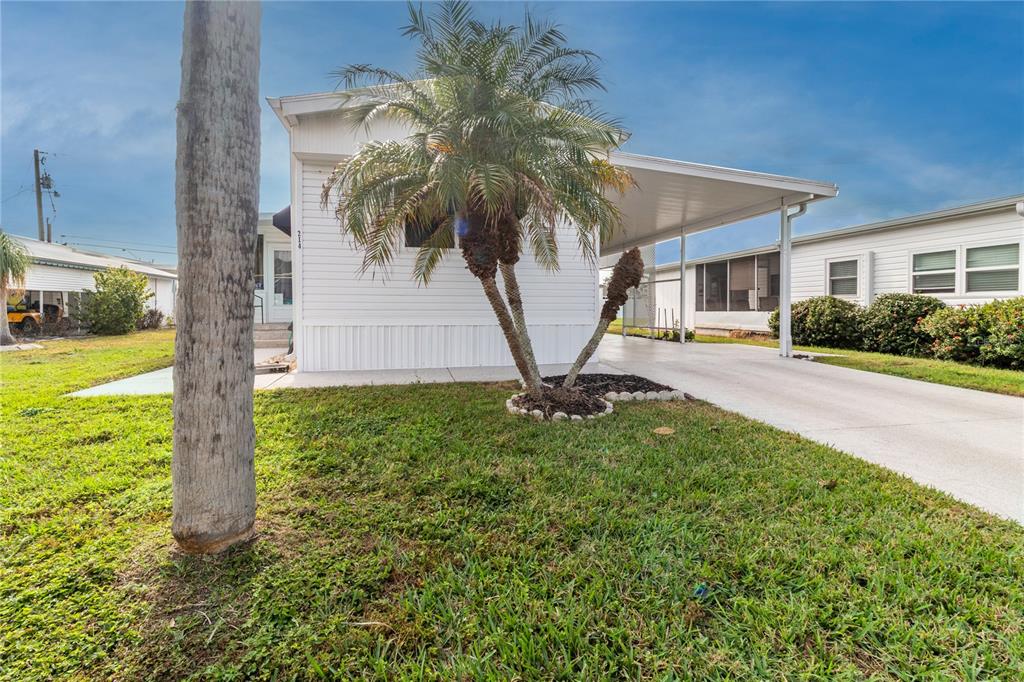 A white mobile home features a palm tree in the front yard and a carport — 214 LEISURE WAY, PALMETTO, FL