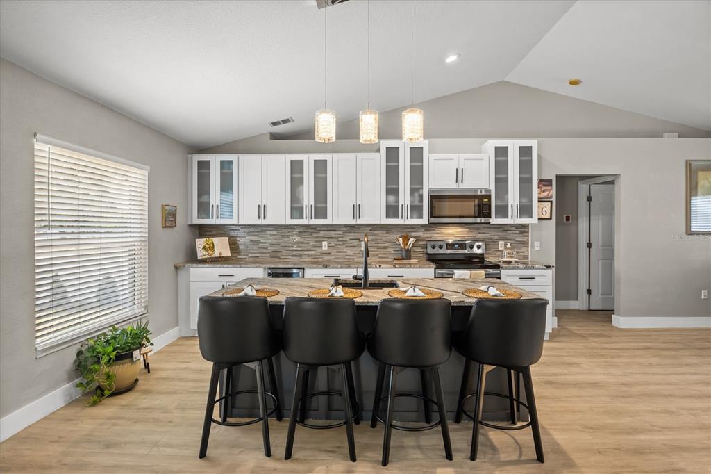 A kitchen features white cabinets, a dark island with four stools, and light wood flooring — 5963 HILLSIDE HEIGHTS DRIVE, LAKELAND, FL