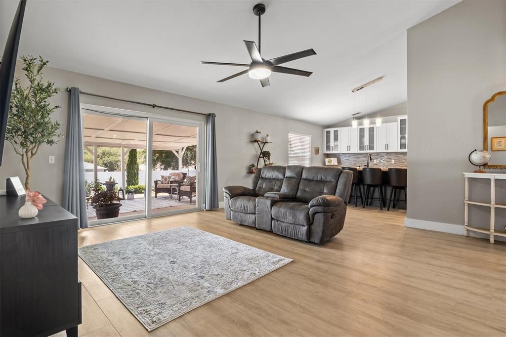 A living room with light wood floors, a grey loveseat, and a sliding glass door — 5963 HILLSIDE HEIGHTS DRIVE, LAKELAND, FL