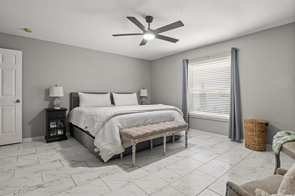 A bedroom features a bed, a bench, a ceiling fan, and white marble-patterned tile flooring — 5963 HILLSIDE HEIGHTS DRIVE, LAKELAND, FL