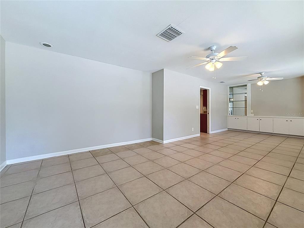 A spacious room features light-colored walls, large beige floor tiles, and two ceiling fans — 7123 WOODFIELD DRIVE, TAMPA, FL