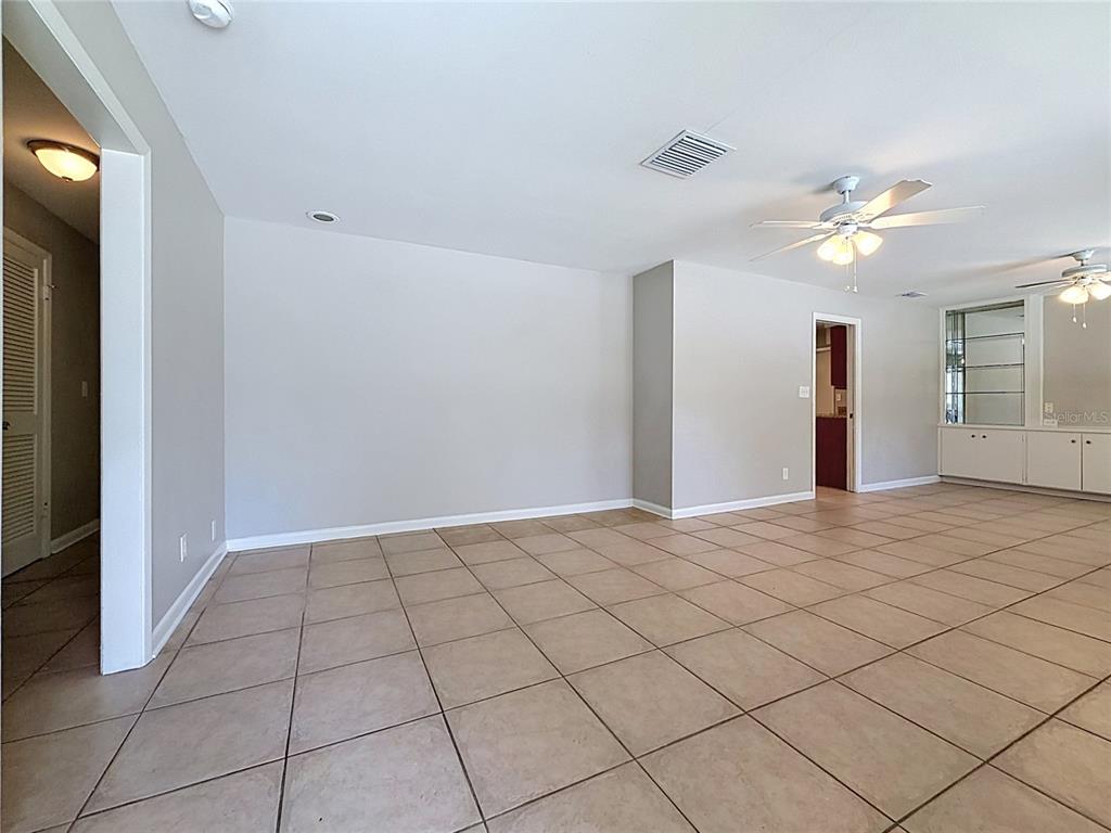 An empty room with beige tile flooring, light gray walls, and two ceiling fans — 7123 WOODFIELD DRIVE, TAMPA, FL