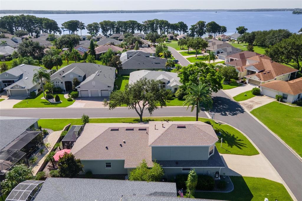 An aerial view shows a suburban neighborhood with houses, green lawns, and a large lake — 5486 BOUNTY CIRCLE, TAVARES, FL