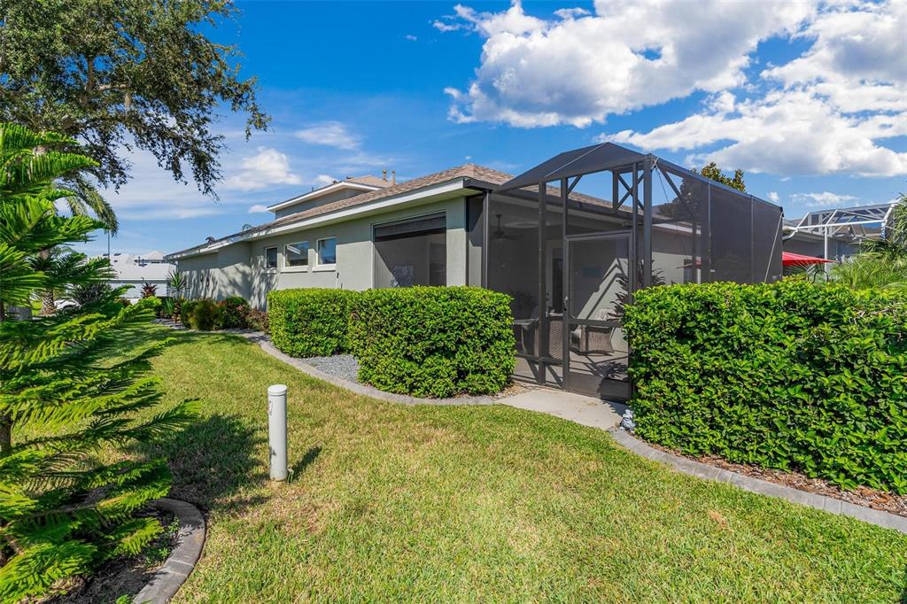 A house exterior features a screened-in lanai, manicured hedges, and a grassy lawn — 5486 BOUNTY CIRCLE, TAVARES, FL