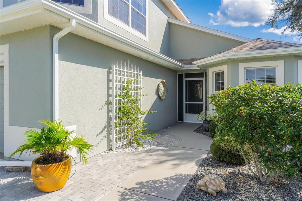 A paved walkway leads to the front entrance of a house with light green stucco walls — 5486 BOUNTY CIRCLE, TAVARES, FL