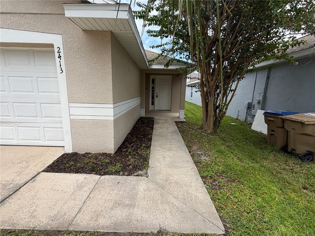 A concrete walkway leads to the front entrance of a tan house with a garage — 2413 RUDDENSTONE WAY, KISSIMMEE, FL