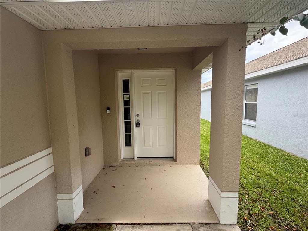 A covered concrete porch leads to a white front door with a side window panel — 2413 RUDDENSTONE WAY, KISSIMMEE, FL