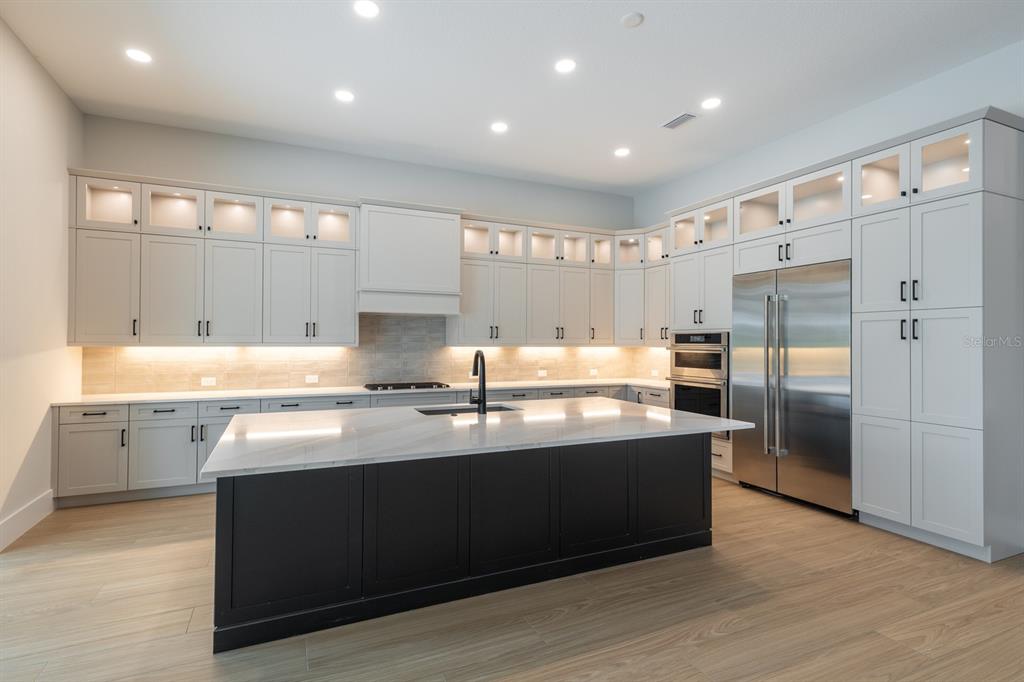 A modern kitchen features a dark island, light cabinetry, stainless steel appliances, and wood flooring — 268 BLUE PEARL CT,, SARASOTA, FL