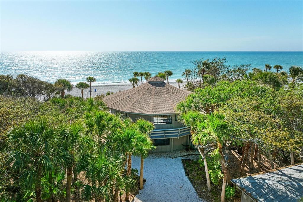 An elevated, octagonal house sits nestled among palm trees near a sandy beach and ocean — 6590 MANASOTA KEY ROAD, ENGLEWOOD, FL