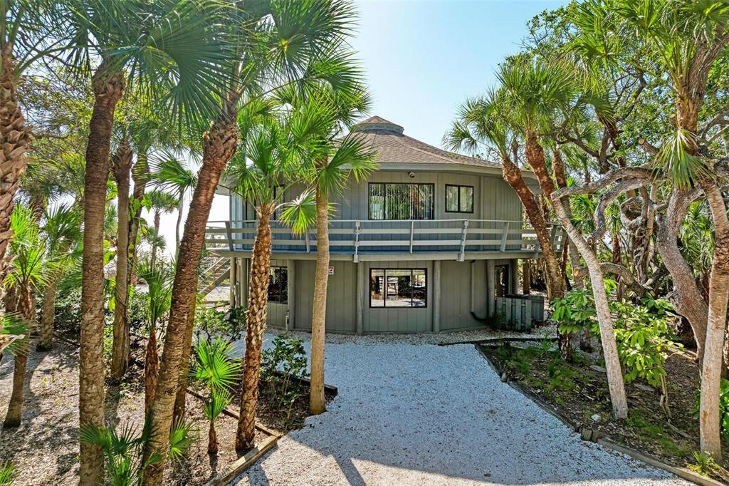 A two-story circular house with a wraparound balcony sits among palm trees and gravel landscaping — 6590 MANASOTA KEY ROAD, ENGLEWOOD, FL