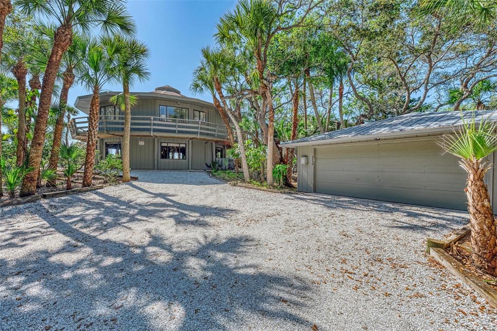 A two-story circular house with a wrap-around balcony stands beside a detached garage — 6590 MANASOTA KEY ROAD, ENGLEWOOD, FL