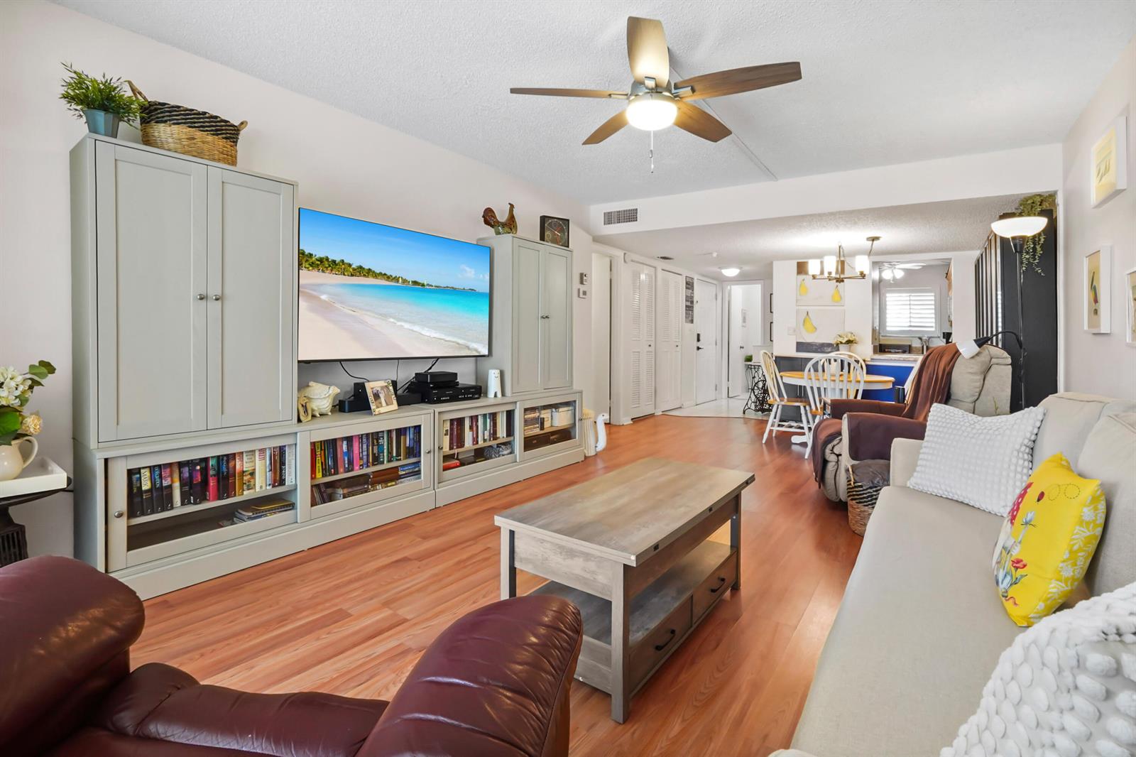 A living room features a large entertainment center, wood-look flooring, and a ceiling fan — 5355 SE Miles Grant Road # 114, Stuart FL 34997, STUART, FL