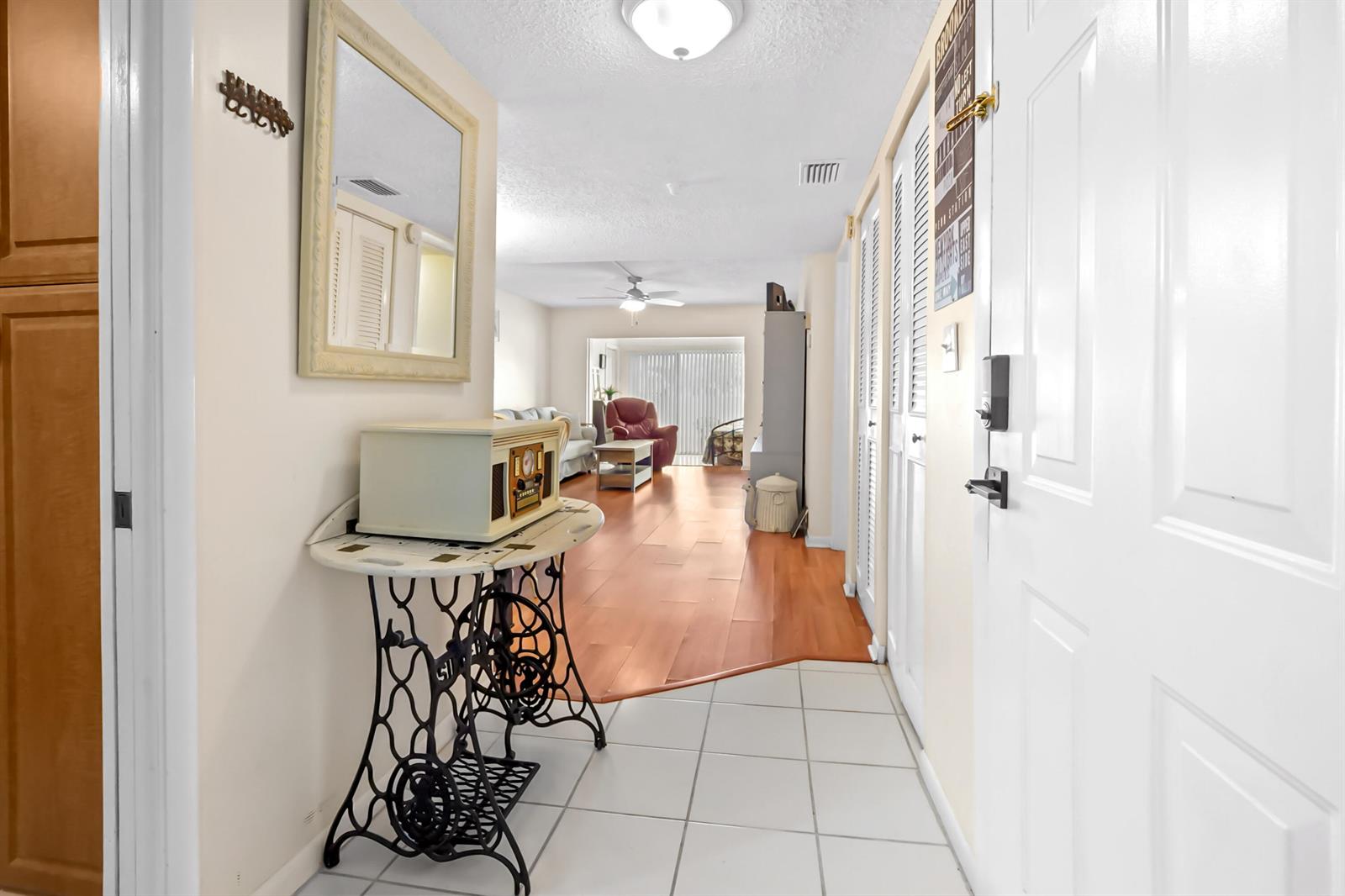 A hallway with a vintage sewing machine table leads into a living room with wood flooring — 5355 SE Miles Grant Road # 114, Stuart FL 34997, STUART, FL