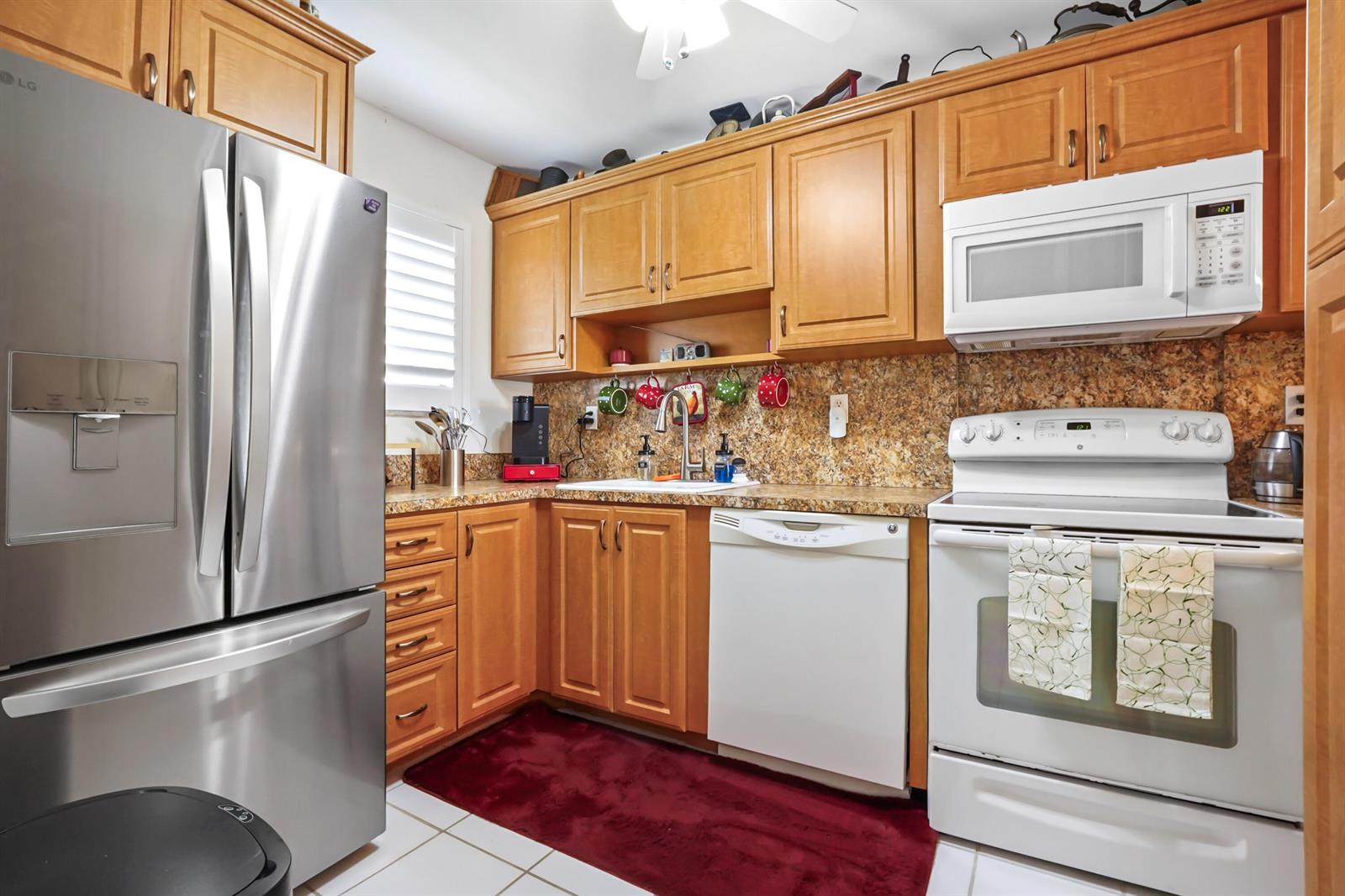 A kitchen features wood cabinets, stainless steel appliances, a white stove, and granite countertops — 5355 SE Miles Grant Road # 114, Stuart FL 34997, STUART, FL